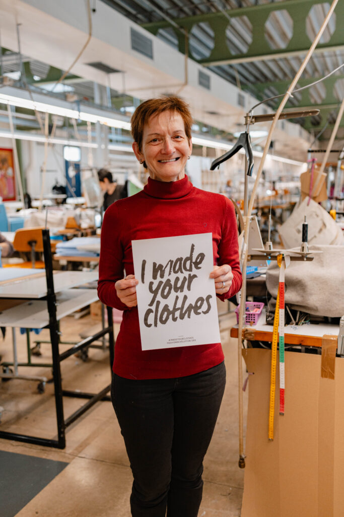 Garment factory worker standing on the factory floor holding a sign reading "I made your clothes"
